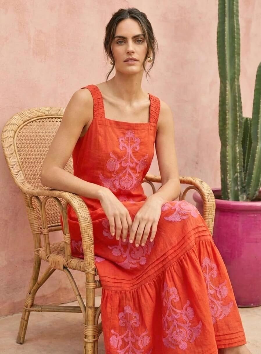 Donna con abito lungo rosso ricamato seduta su sedia in ambiente urbano