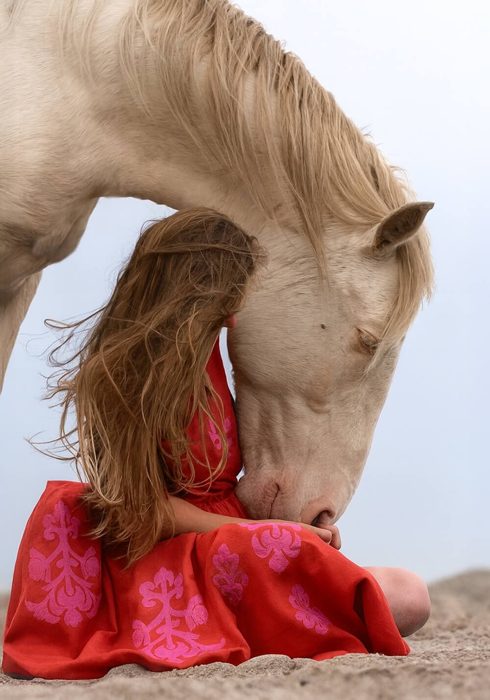 Donna con abito rosso ricamato accanto a cavallo bianco